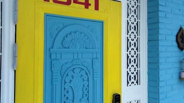 Een deur met het nummer 1941, een decoratief blauw patroon op de deur, en een witte decoratieve paneel aan de muur.
