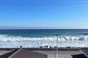 A coastal view with waves crashing against a concrete barrier, a clear sky, and a distant horizon.