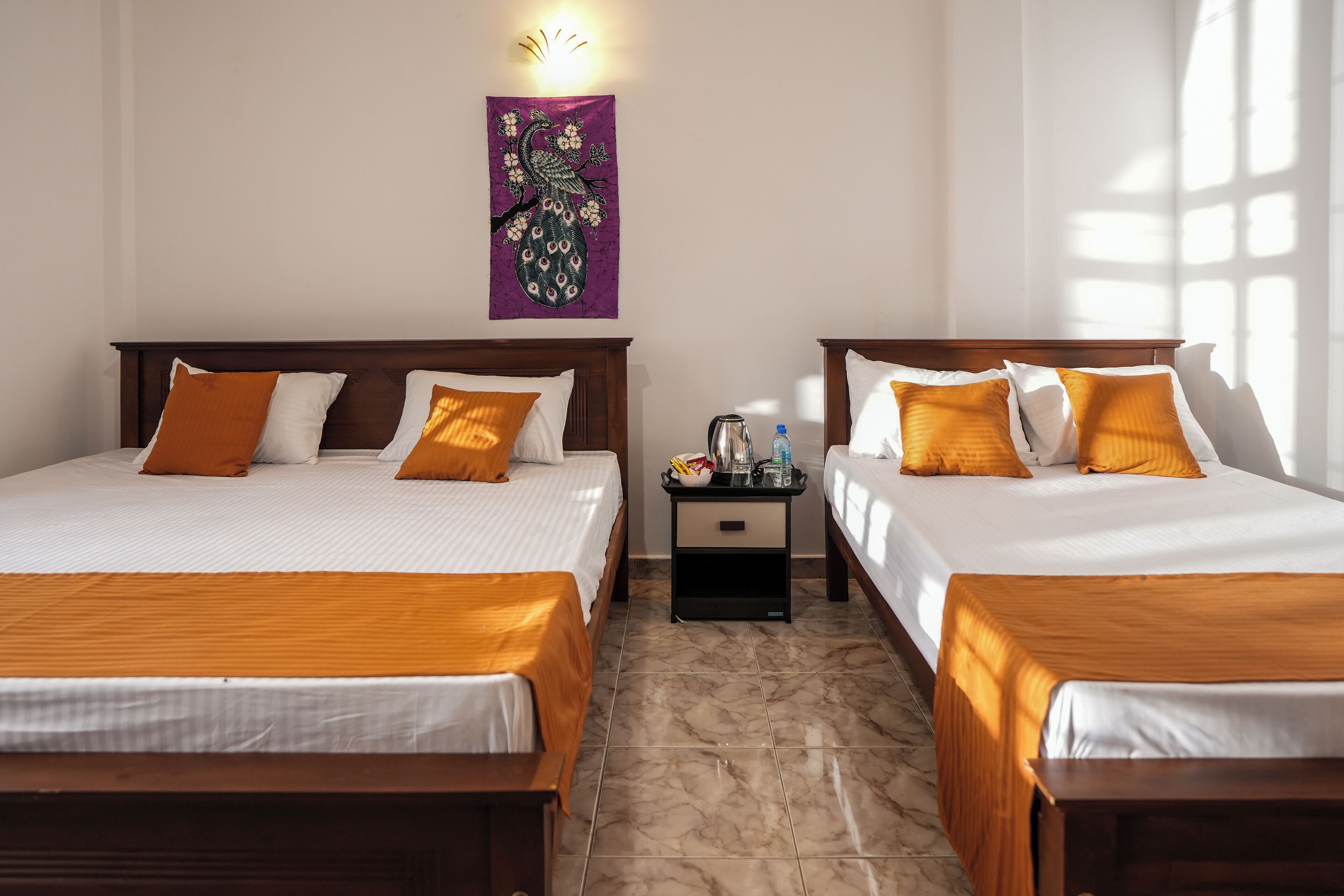 A hotel room with two beds, a nightstand, a wall-mounted light, and a decorative wall hanging.