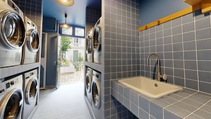 A laundry room with multiple washing machines, a sink, and a view of the outside.