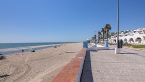 A beach with a paved walkway, palm trees, and buildings in the background. - Holiday Home 'Primera Linea En Matalascañas' with Sea View, Wi-Fi and Air Conditioning (Almonte)
