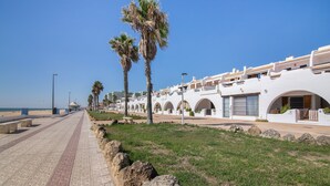 A coastal hotel with a paved walkway, palm trees, and white buildings with arched windows. - Holiday Home 'Primera Linea En Matalascañas' with Sea View, Wi-Fi and Air Conditioning (Almonte)