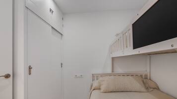 A bedroom with a single bed, a white wardrobe, a mounted television, and a door with a handle.