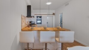 A modern kitchen with a central island, white bar stools, and a view into the dining area. - Holiday Home 'Primera Linea En Matalascañas' with Sea View, Wi-Fi and Air Conditioning (Almonte)