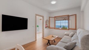 A modern living room with a flat-screen TV, a sofa, a small table, and a window with a view. - Holiday Home 'Primera Linea En Matalascañas' with Sea View, Wi-Fi and Air Conditioning (Almonte)