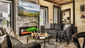 A cozy living room with a stone fireplace, a large flat-screen TV, and comfortable seating.