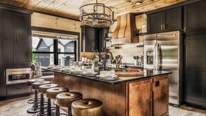 A modern kitchen with dark cabinets, stainless steel appliances, and a wooden ceiling.
