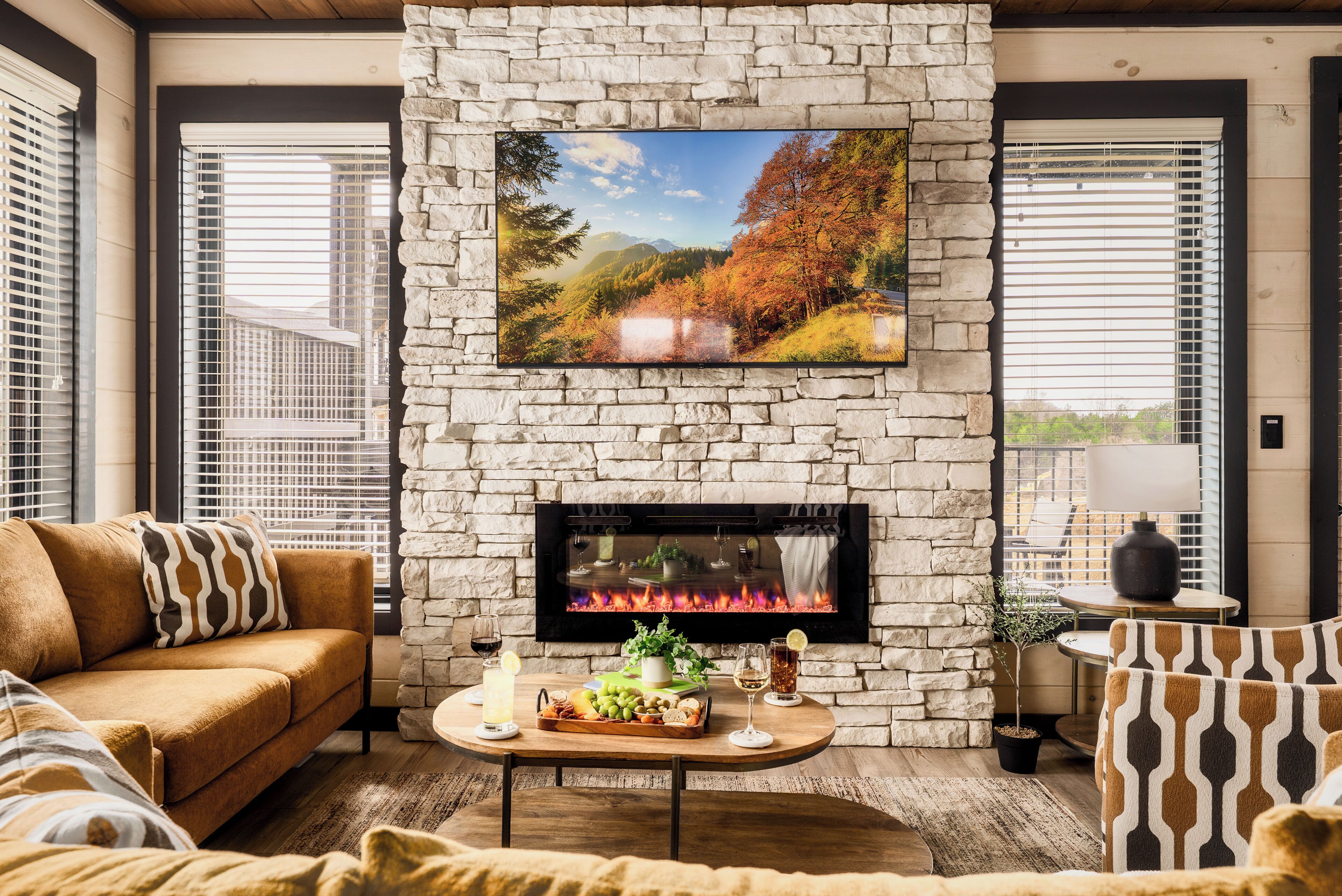A cozy living room with a stone fireplace, a large TV mounted above it, and a comfortable sofa.