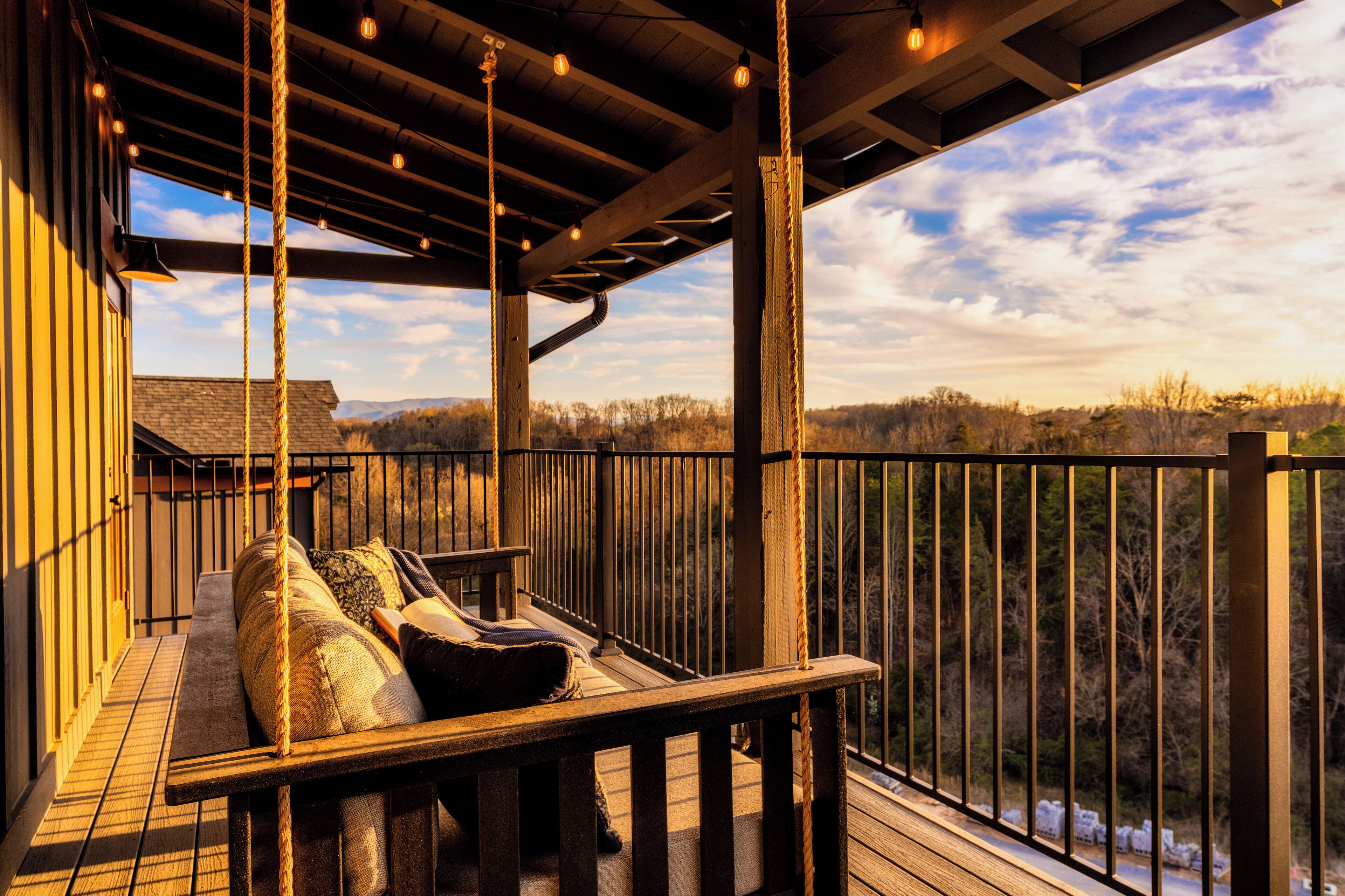 A wooden deck with a bench and pillows, overlooking a forested landscape.