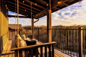 Une terrasse en bois avec un banc et des coussins, offrant une vue sur un paysage boisé.