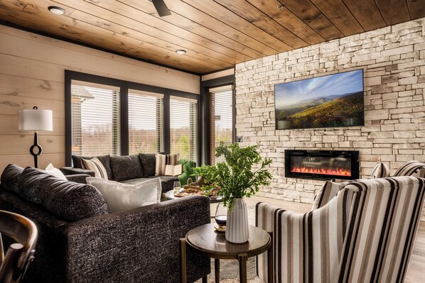 A cozy living room with a stone wall, a fireplace, and a large TV.