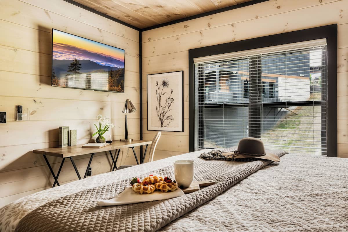 Ein gemütliches Schlafzimmer mit einem Bett, einem Nachttisch mit Lampe, einem gerahmten Bild und einem Fenster mit Jalousien.