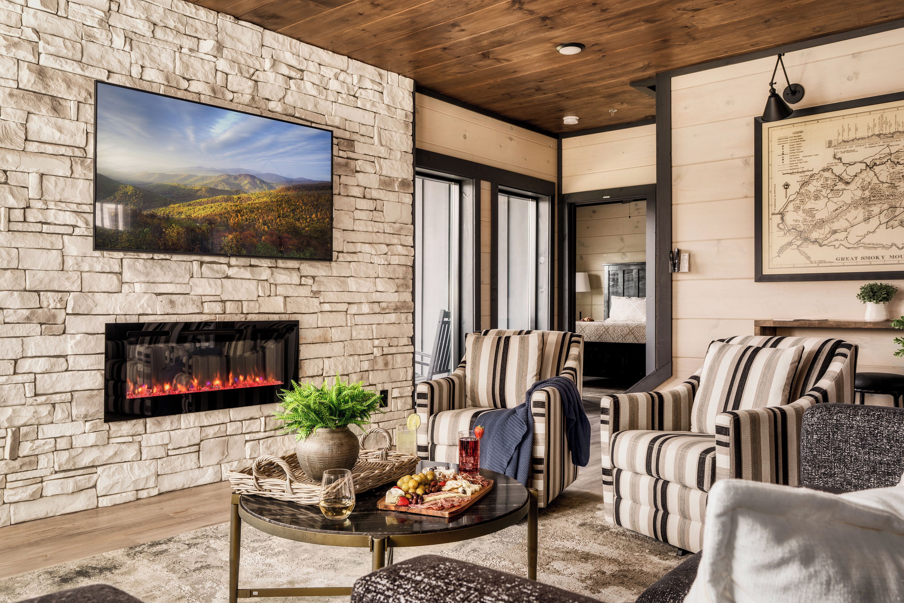 A cozy living room with a stone wall, a fireplace, a large TV, and striped furniture.