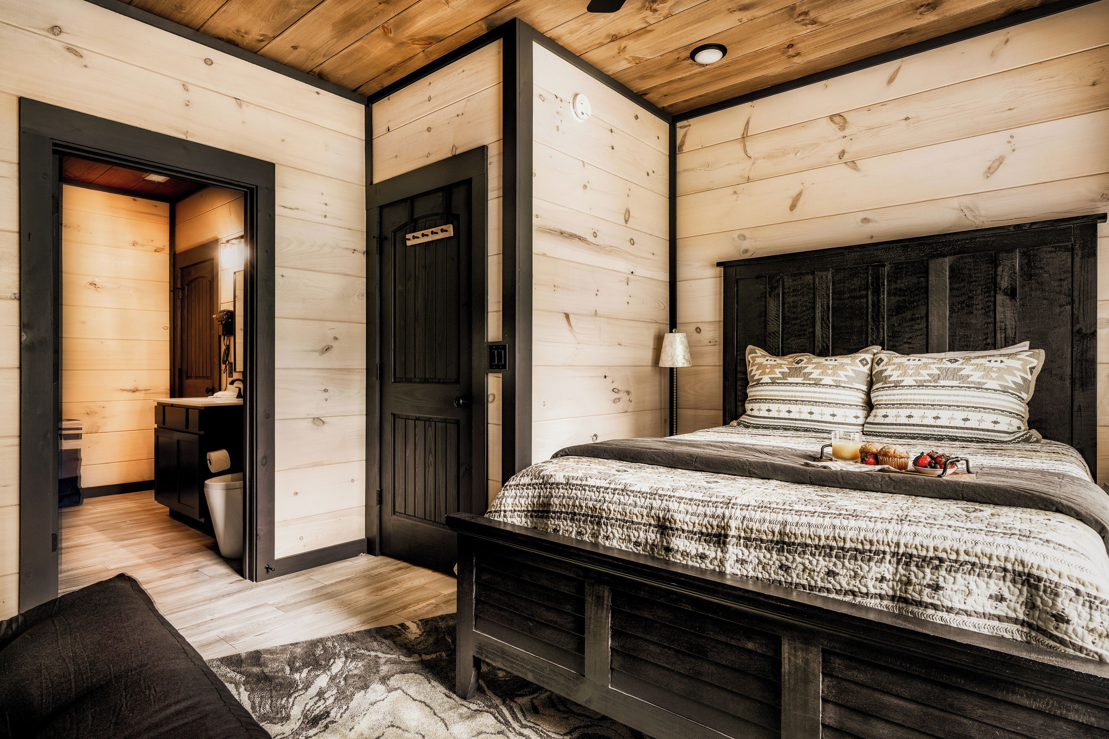 A wooden cabin interior with a bed, a bathroom, and a small kitchen area.