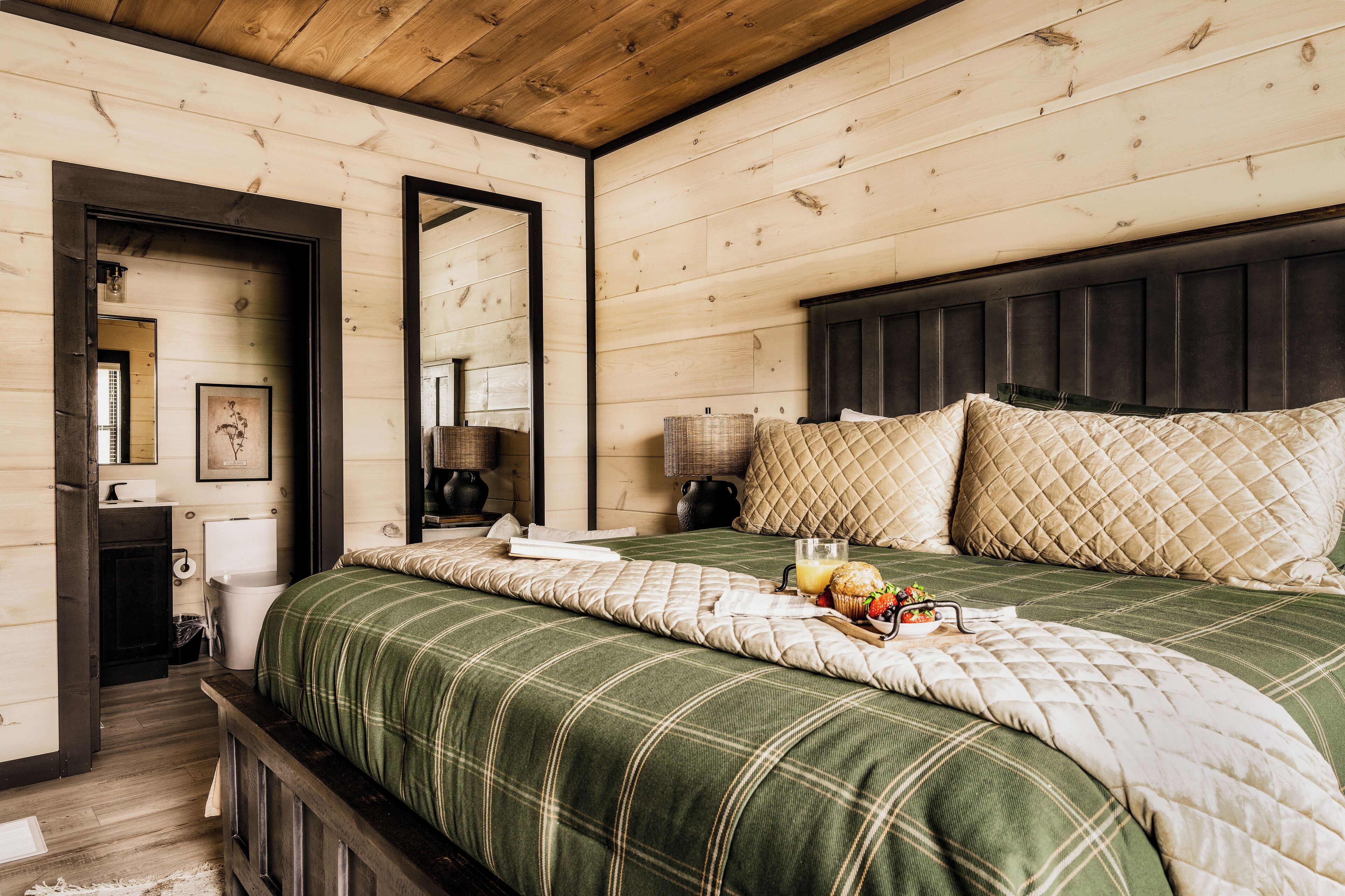 A wooden-paneled bedroom with a bed, pillows, a bedside table, and a mirror.
