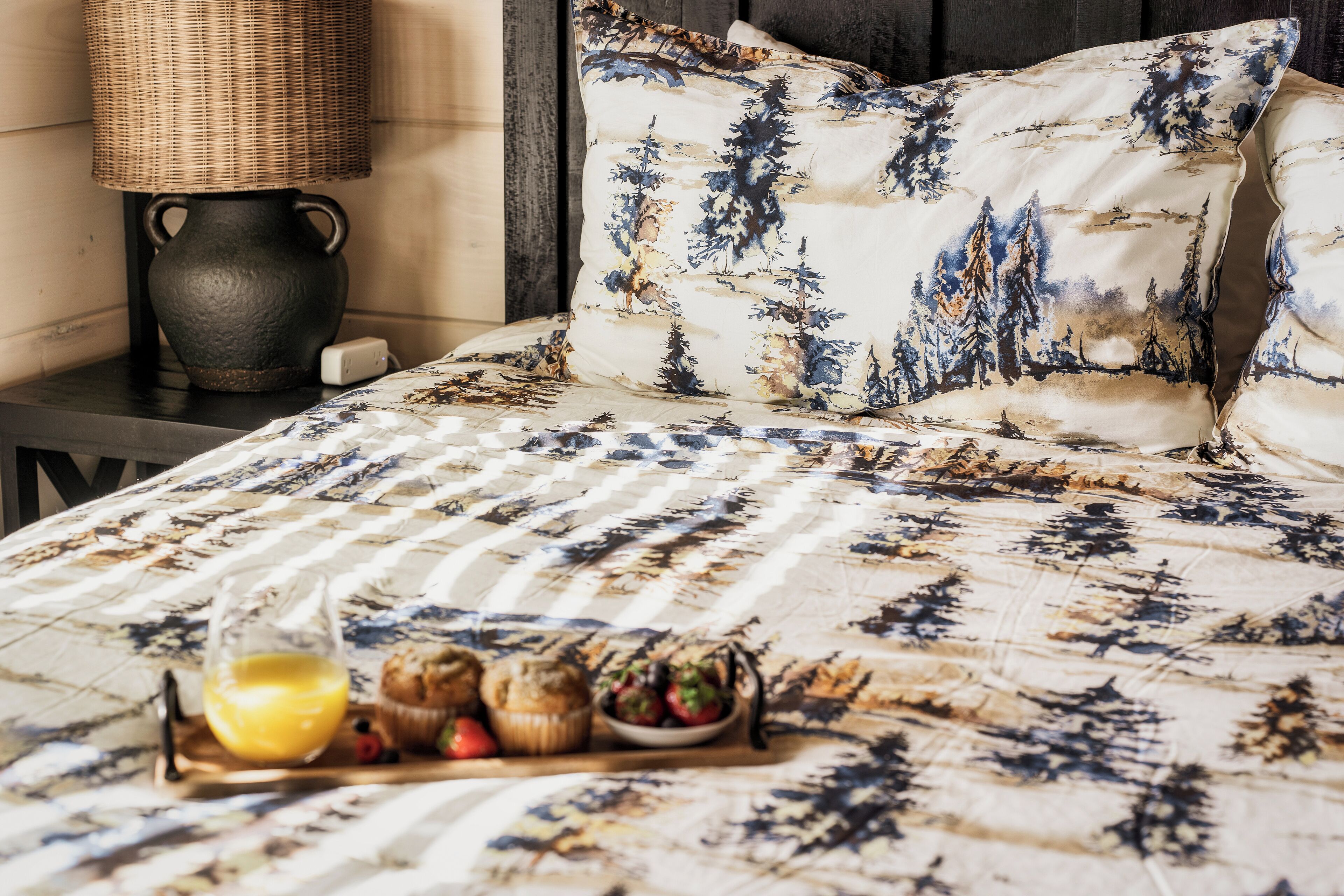 A bed with a patterned bedspread, a bedside table with a lamp, and a tray with breakfast items.
