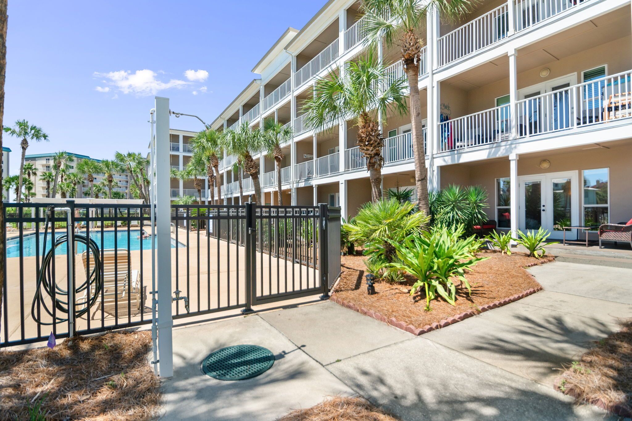 A multi-story hotel with balconies, a swimming pool, and landscaped areas with palm trees.
