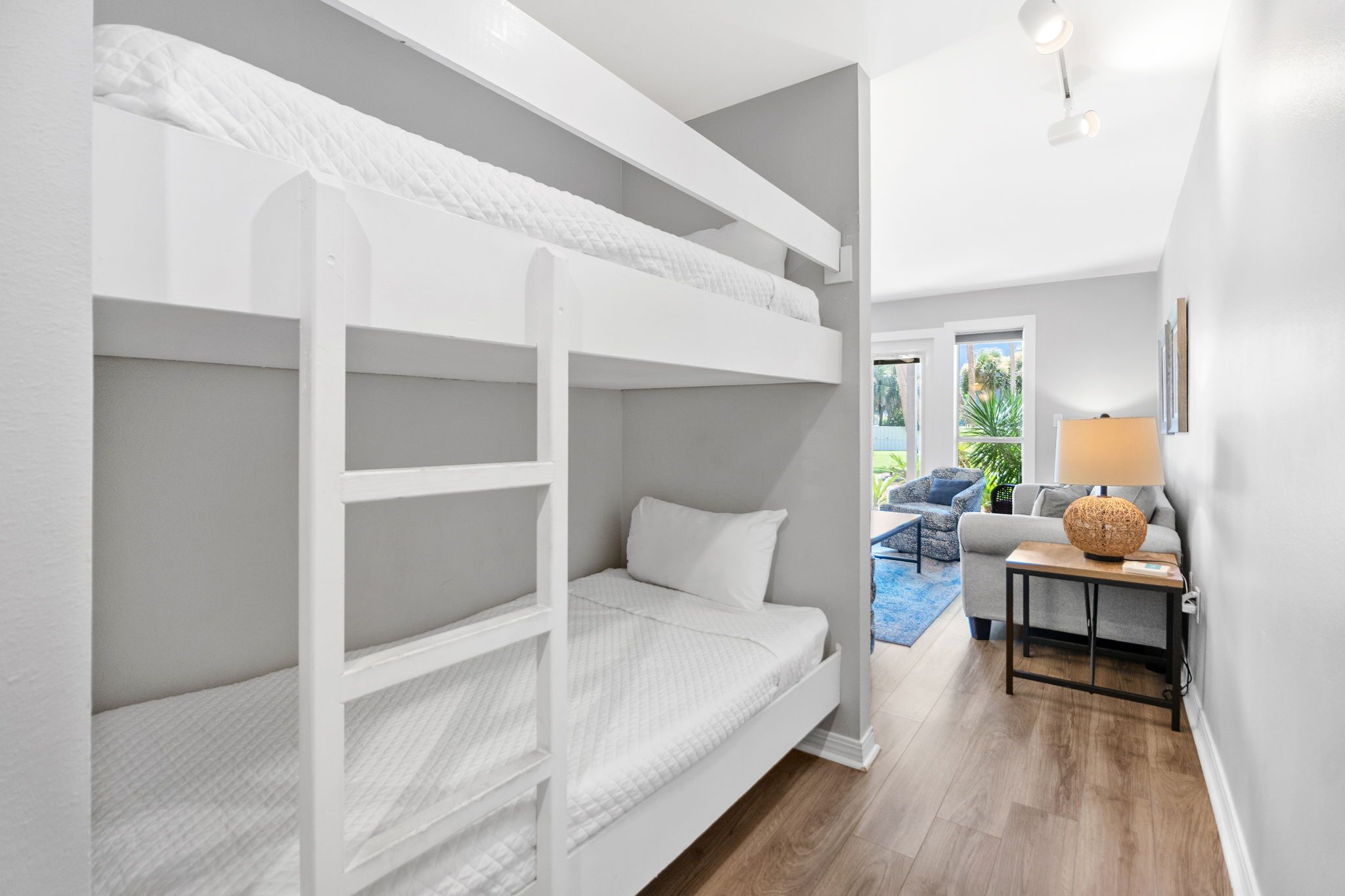 A bunk bed room with a grey sofa and a lamp in the corner.