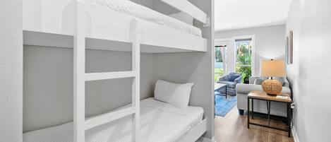 A bunk bed room with a grey sofa and a lamp in the corner.