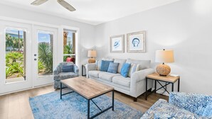 Un salón amplio con ventilador de techo, un sofá de color claro, un sillón estampado, una mesa de centro de madera y dos mesitas de noche con lámparas.