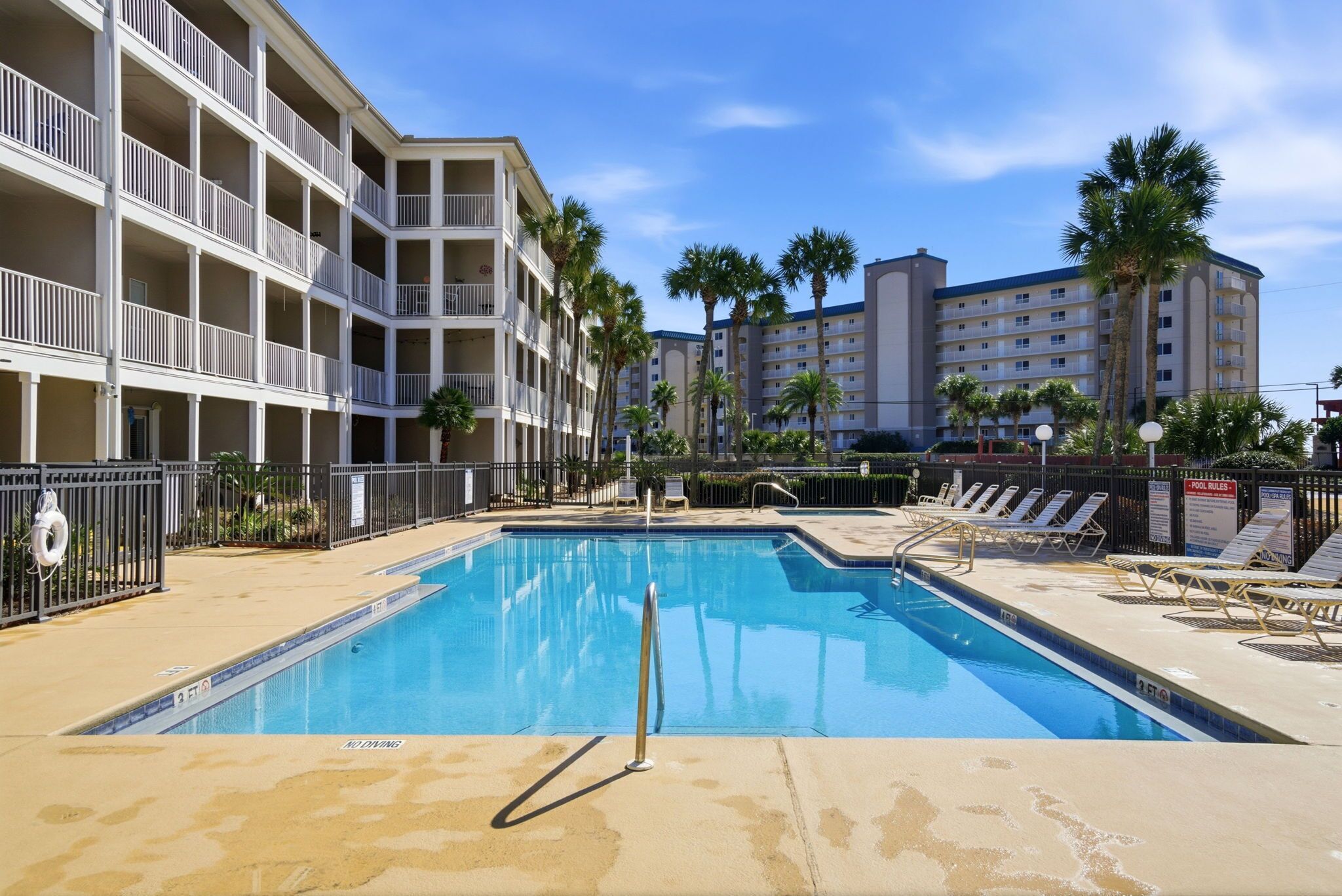 A swimming pool with lounge chairs, a lifebuoy, and a pool fence.