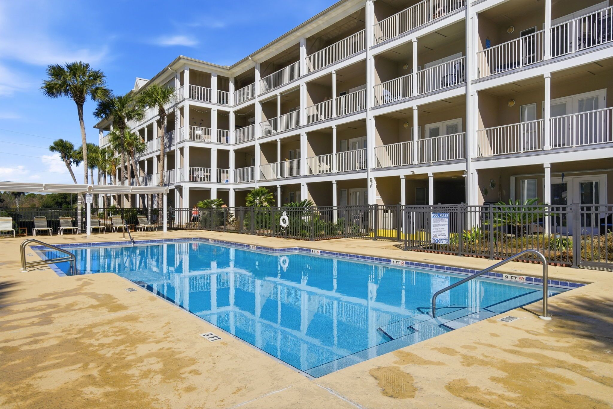 A multi-story hotel with a swimming pool, balconies, and palm trees.