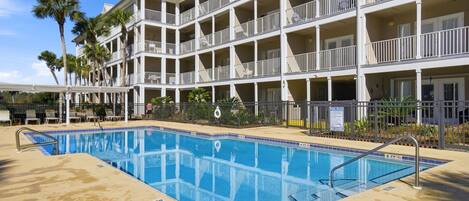 A multi-story hotel with a swimming pool, balconies, and palm trees.
