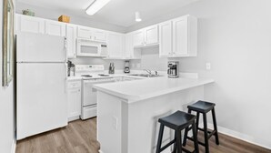 Una cocina moderna con armarios blancos, una isla central con taburetes, microondas, estufa y cafetera.