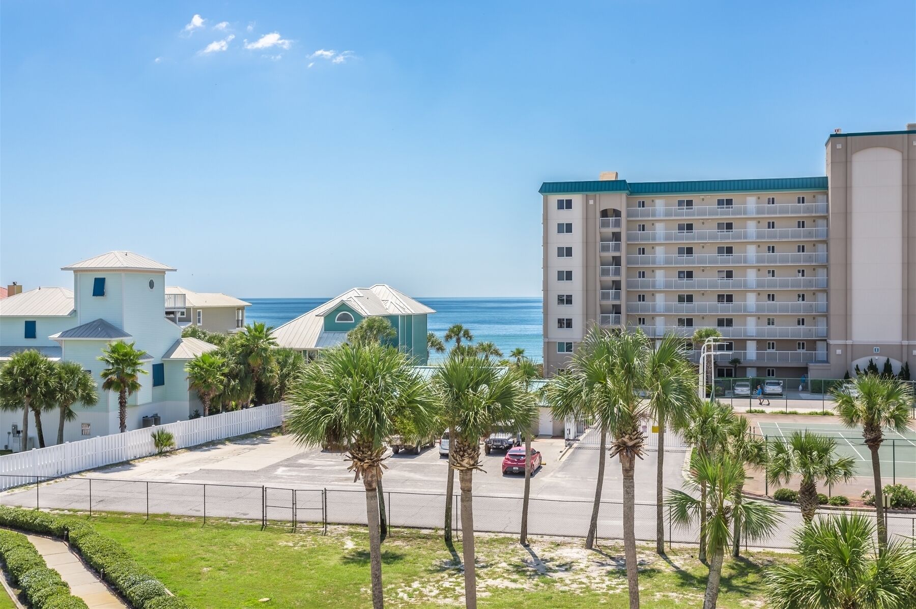 Een hotel aan de kust met een parkeerplaats, palmbomen en uitzicht op zee.
