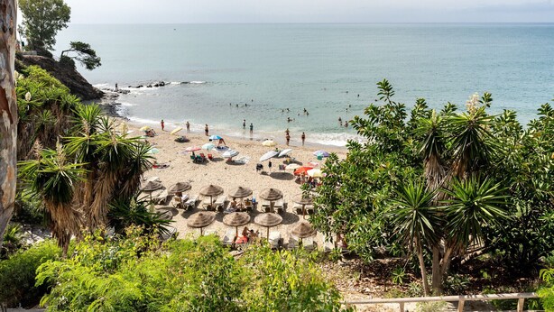 Una spiaggia con lettini e ombrelloni, una costa rocciosa e vista sul mare.