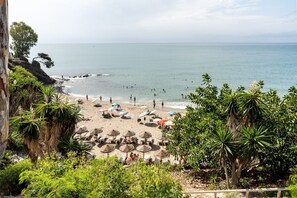 Une plage avec des transats et des parasols, une côte rocheuse et une vue sur la mer.