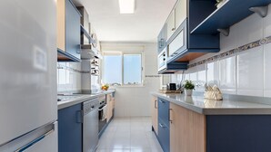 Una cucina angusta con mobili blu, una finestra con vista e un piano di lavoro con una macchina da caffè e una pianta.