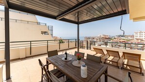 Un'area salotto esterna coperta con tavolo, sedie e vista sulla città e sul mare.