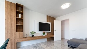 Un soggiorno moderno con una TV a schermo piatto montata su una parete in legno, un divano grigio e un pavimento in marmo.