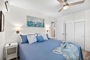 A bedroom with a bed, a ceiling fan, a painting, bedside lamps, and a closet.
