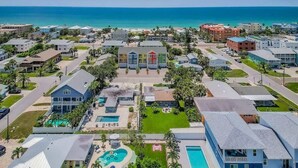 Ein Wohngebiet mit einem zentralen Gebäude, einem mehrstöckigen Bauwerk mit flachem Dach, umgeben von eingeschossigen Häusern, einem Schwimmbad und Blick auf den Ozean.
