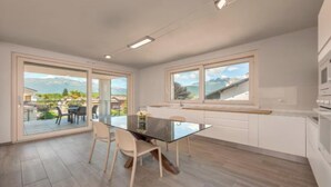 Ett modernt kök med ett matbord i glas, vita köksskåp och stora fönster med utsikt över bergen.