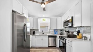 Una cocina moderna con gabinetes blancos, electrodomésticos de acero inoxidable, lavavajillas y ventilador de techo.