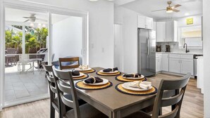 Una cocina moderna con armarios blancos, un refrigerador de acero inoxidable y un comedor con una mesa lista para cuatro.