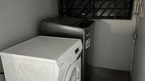 Ein kleiner Waschbereich mit Waschmaschine und Trockner, ein Fenster mit Gitterrost und eine Tür mit Griff.