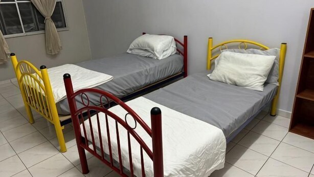 Quarto com duas camas de solteiro, uma cadeira e uma janela com cortinas.