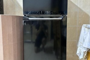 A kitchen with a black stove, a tiled backsplash, and a towel hanging on the wall. - JL Homestay Bahau (Bahau)