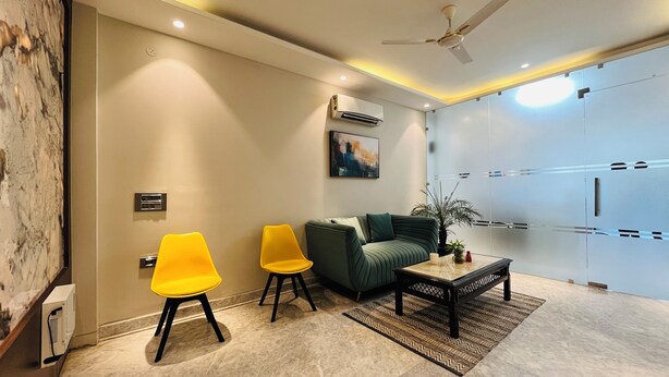 A modern living room with a sofa, two yellow chairs, a coffee table, and a ceiling fan. - EXE Banquet and Conference Hall Gurgaon (Gurugram)