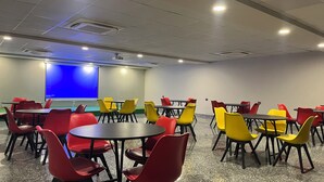 A conference room with multiple tables and chairs, a projector screen, and a whiteboard. - EXE Banquet and Conference Hall Gurgaon (Gurugram)
