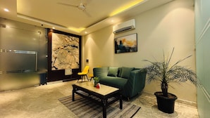 A modern living room with a green sofa, a coffee table, a potted plant, and a yellow chair. - EXE Banquet and Conference Hall Gurgaon (Gurugram)