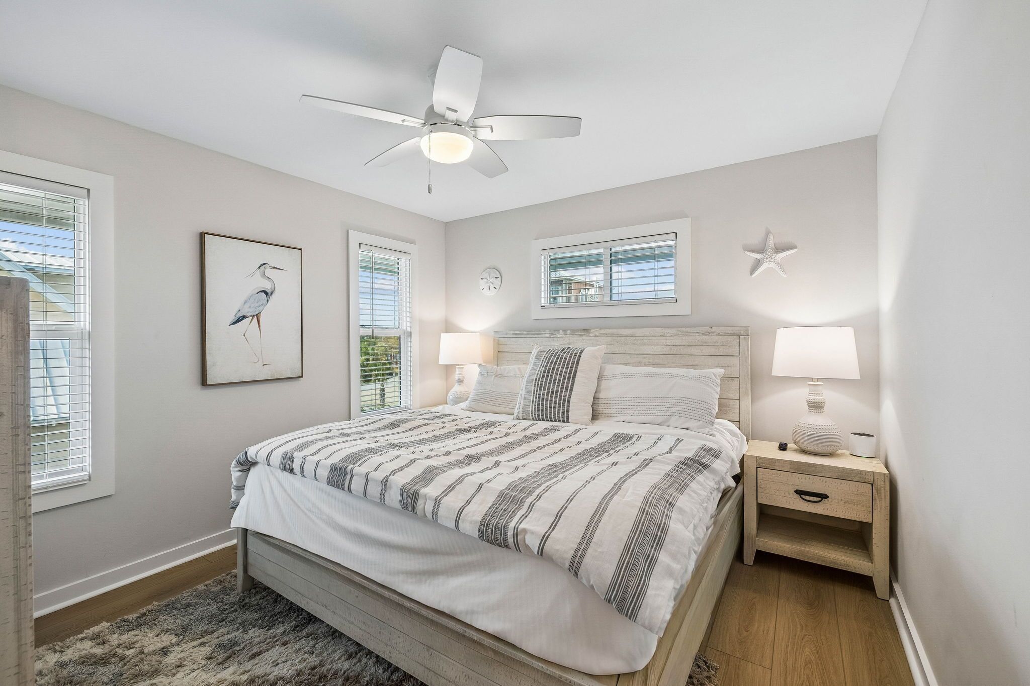 Une chambre à coucher avec un lit, des lampes de chevet, un ventilateur de plafond et des œuvres d’art accrochées aux murs.