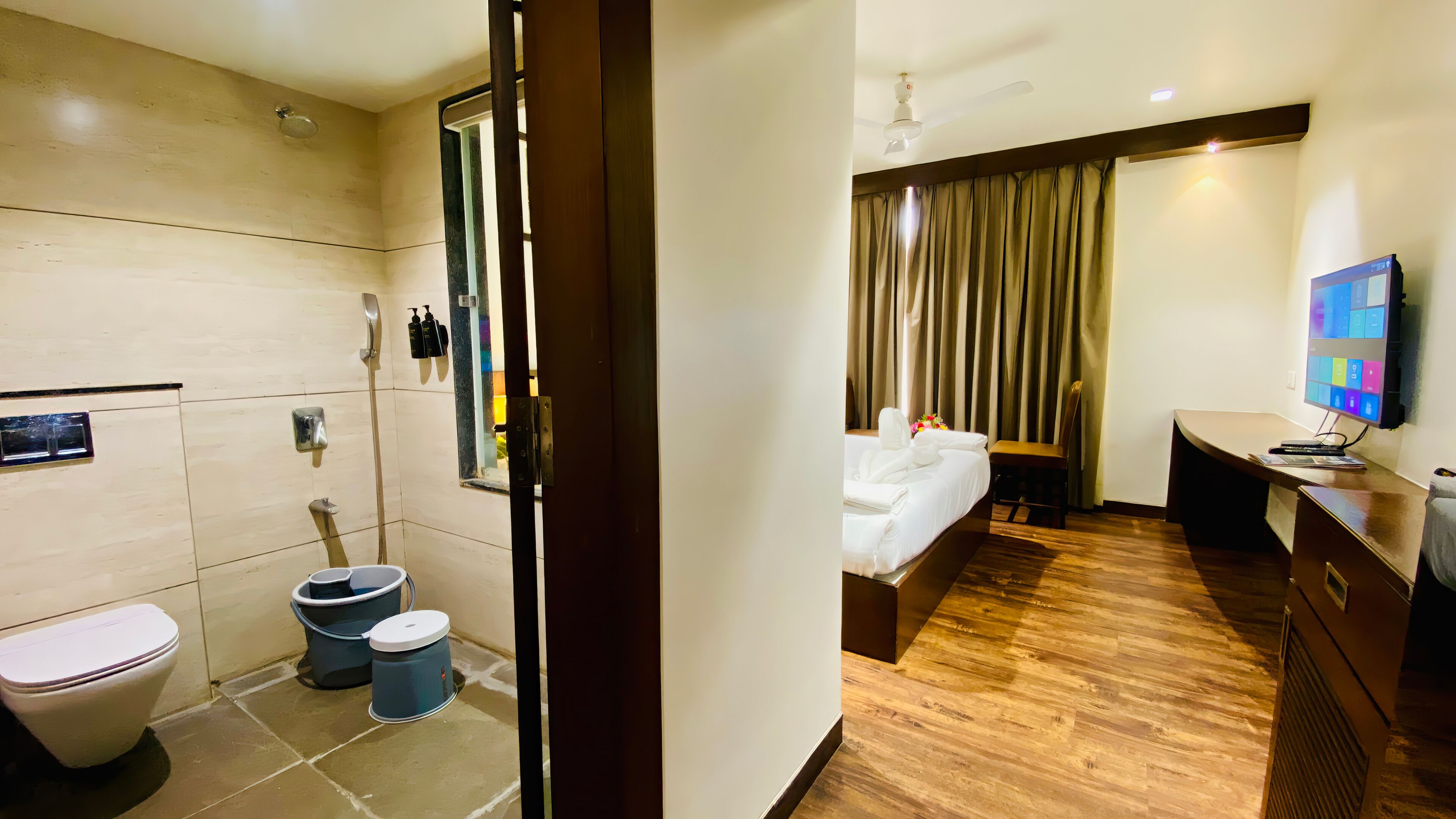 A hotel room with a bathroom, a bed, a desk, and a TV.