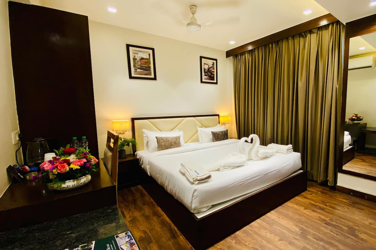 A hotel room with a large bed, two wall-mounted lamps, a mirror, and a wooden floor.