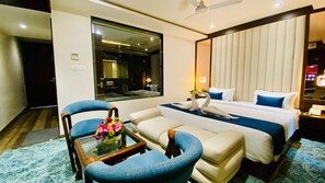 Habitación de hotel con cama, dos sillones, una mesita con un jarrón de flores, un espejo grande y una mesita de noche con un teléfono.
