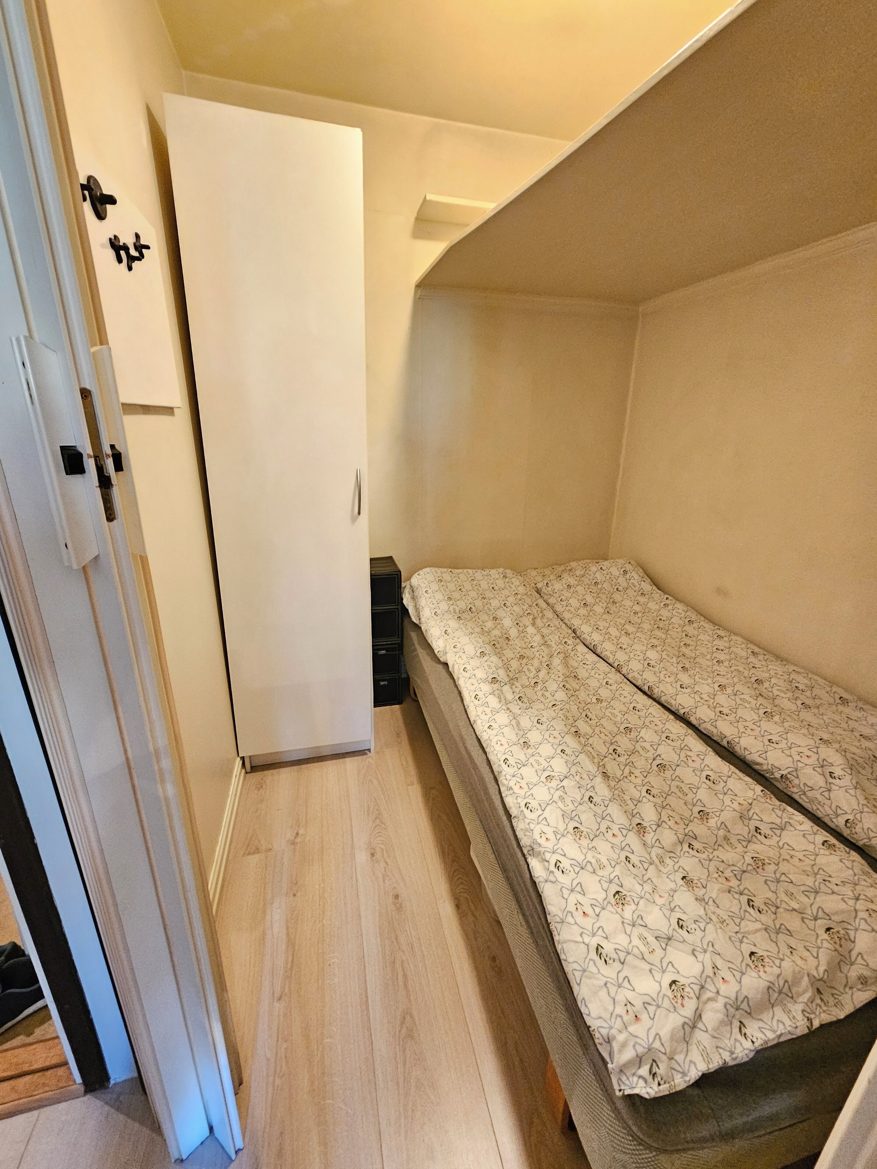 Ein kleines Zimmer mit einem Bett, einem Kleiderschrank und einer Tür.